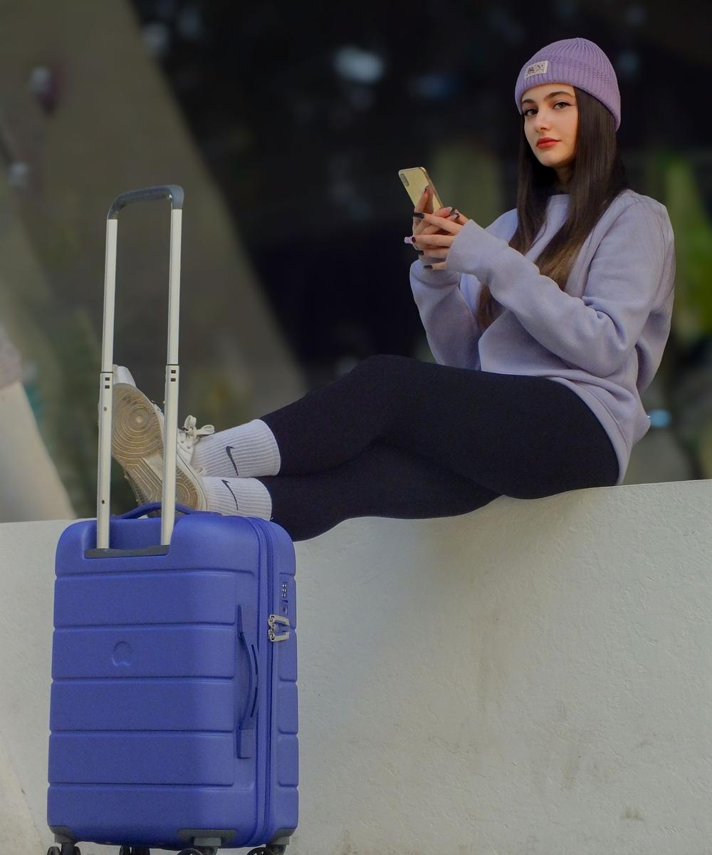 A young traveler with a suitcase checks her phone